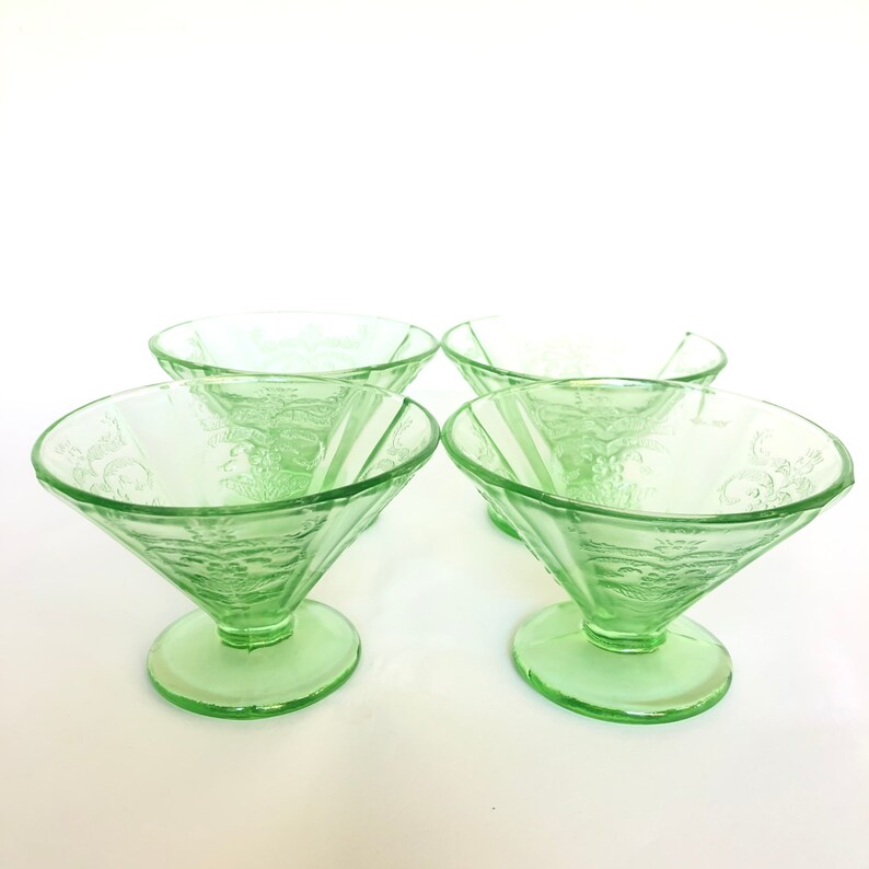 May include: Set of four green glass dessert bowls with a floral design. The bowls are made of a clear glass with a green tint and have a scalloped edge.