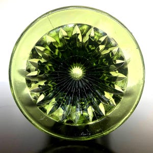 Puede incluir: Vista superior de un objeto de vidrio verde con una base circular y un patr&oacute;n detallado en forma de estrella en el centro. El vidrio tiene un acabado brillante y el color es un verde vibrante y transparente.