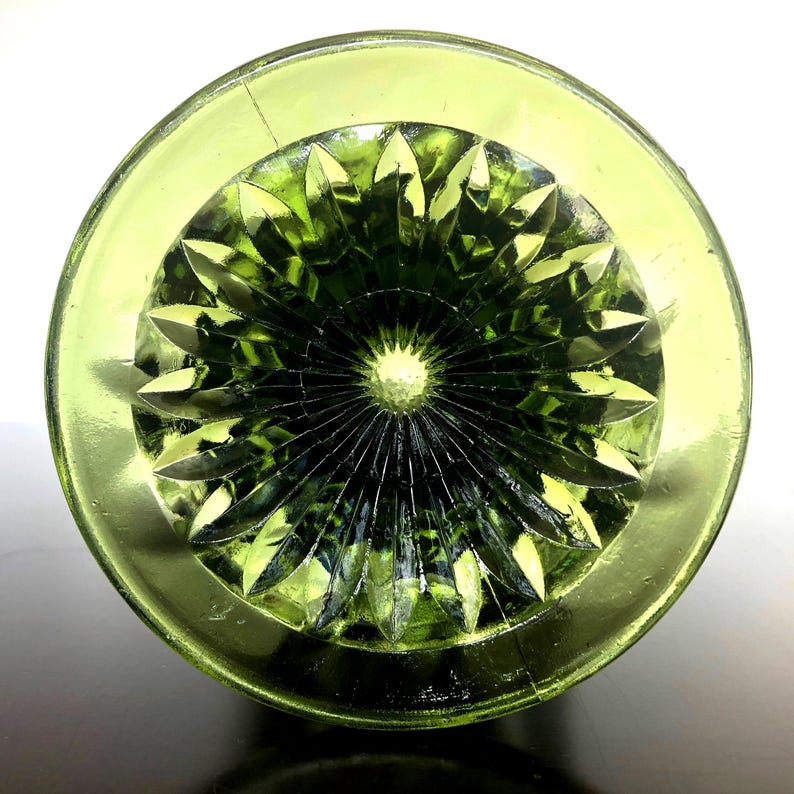 Puede incluir: Vista superior de un objeto de vidrio verde con una base circular y un patr&oacute;n detallado en forma de estrella en el centro. El vidrio tiene un acabado brillante y el color es un verde vibrante y transparente.