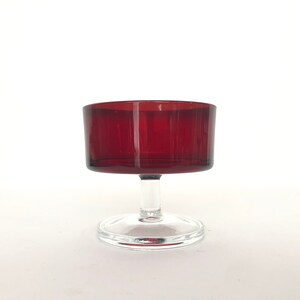 Puede incluir: Una copa de vidrio transparente con tallo y un cuenco de color rojo oscuro. La copa es perfecta para servir cócteles o postres.
