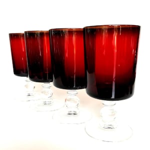 May include: Four red wine glasses with clear stems and bases. The glasses have a deep red colour that fades to black at the bottom. The stems have a decorative, bulbous design. The glasses are arranged in a row.
