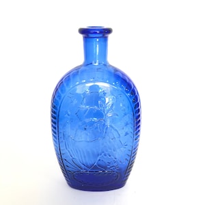 May include: A cobalt blue glass bottle with an embossed design of a bird and floral motif. The bottle has a rounded body and a narrow neck.