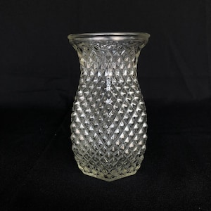 Puede incluir: Un jarrón de vidrio transparente con un patrón de forma de diamante. El jarrón es alto y delgado con una base redonda.