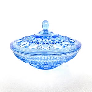 Op de afbeelding: Een lichtblauwe glazen snoepschaal met deksel. De schaal heeft een ronde vorm met een getextureerd, diamantpatroon deksel en een decoratieve basis. Het deksel heeft een kleine, afgeronde handgreep. De snoepschaal is gemaakt van transparant glas.