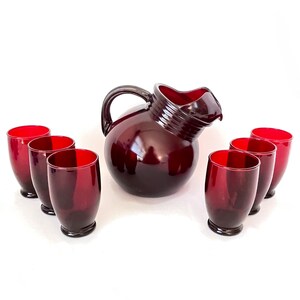 May include: A set of six ruby red glass tumblers and a matching pitcher. The pitcher has a rounded body and a wide spout.