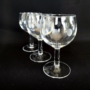 Könnte beinhalten: Drei klare Weingläser mit geätzten Polka-Dot-Mustern. Die Gläser haben eine runde Schalenform, einen schlanken Stiel und einen kreisförmigen Fuß. Sie sind in einer Reihe vor einem schwarzen Hintergrund angeordnet.