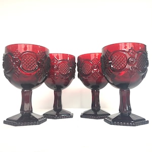 Puede incluir: Juego de cuatro copas de vidrio rojo con un patrón de diamante. Las copas tienen un tallo y una base de vidrio transparente.