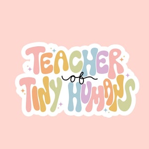 May include: A sticker with the text "TEACHER of TINY HUMANS" in a retro font, with pastel colors on a pink background. The sticker has a white border and star accents. The "oak hill design co" logo is at the bottom.