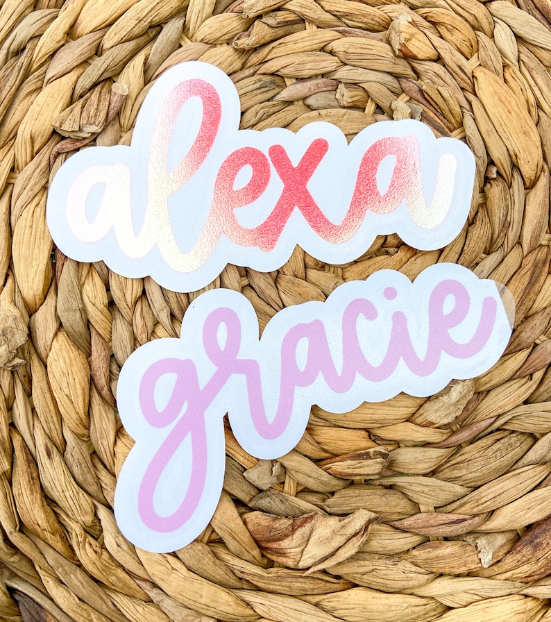 May include: Two die-cut stickers with names. The top sticker says "alexa" in a cursive font with a gradient of pink and gold. The bottom sticker says "gracie" in a pink cursive font. Both stickers have a white border.