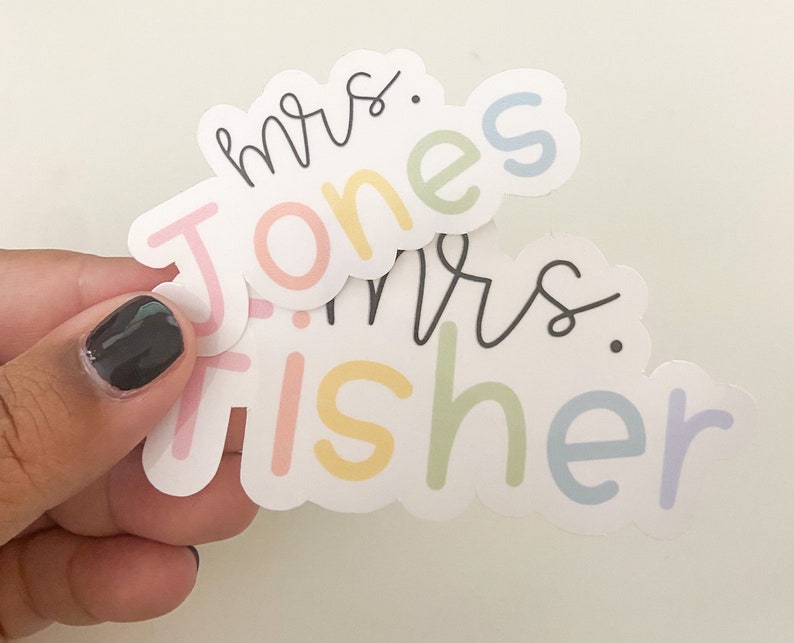 Peut inclure: Deux autocollants aux couleurs pastel sont tenus dans une main. Les autocollants pr&eacute;sentent les noms "mrs. Jones" et "mrs. Fisher" dans un m&eacute;lange d'&eacute;criture cursive et de lettres en bloc. Les lettres sont de couleurs pastel.