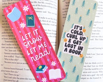 May include: Two decorative bookmarks. One is pink with the text "LET IT SNOW LET ME READ" and illustrations of books and flowers. The other is light green with the text "IT'S COLD, CURL UP & GET LOST IN A BOOK" and tree illustrations.