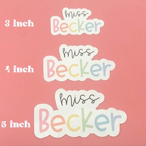 Peut inclure: Trois autocollants avec le texte "miss Becker" dans une palette de couleurs pastel arc-en-ciel. Les autocollants mesurent 7,6, 10,2 et 12,7 cm. Le fond est rose uni. Les autocollants sont probablement destin&eacute;s aux enseignants ou aux &eacute;l&egrave;ves.