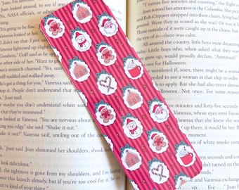 May include: A red and white Christmas-themed bookmark with a repeating pattern of gingerbread houses, snowmen, Santa Claus, and candy canes. The bookmark is rectangular and has a vertical striped background.