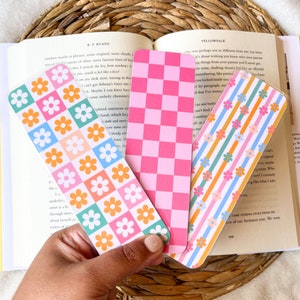 May include: Three colorful bookmarks with floral and checkered patterns. One bookmark features a grid of orange and white flowers on a teal, pink, and orange background. Another has a pink checkerboard design, and the third has stripes with flowers.