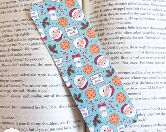 May include: A rectangular bookmark with a light blue background featuring a repeating pattern of Santa Claus faces, cookies, candy canes, milk cartons, and letters that say "Dear Santa".