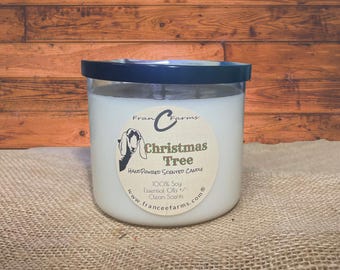 May include: A white scented candle in a clear glass jar with a black lid. The circular label features a goat illustration and the text: Franc C Farms, Christmas Tree, Hand Poured Scented Candle, 100% Soy, Essential Oils, Clean Scents, www.franceefarms.com.
