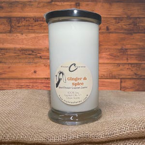 May include: A white candle in a clear glass jar with a black lid. The label on the jar says "Fran C Farms Ginger & Spice Hand Poured Scented Candle 100% Soy Essential Oils Clean Scents www.franceefarms.com".
