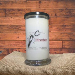 May include: A white candle in a clear glass jar with a black lid. The jar has a label with a goat illustration and the text "Fran C Farms Fireside 100% Soy Candles Pure Scents/Essential Oils www.francfarms.com Rocky Mount, NC".