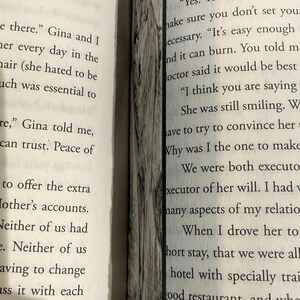 Puede incluir: Libro abierto con texto en p&aacute;ginas blancas. Un marcap&aacute;ginas decorativo de madera se coloca entre las p&aacute;ginas. El marcap&aacute;ginas tiene un aspecto texturizado gris y marr&oacute;n.
