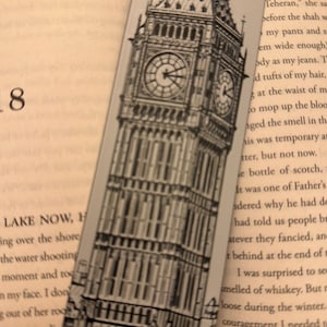 May include: A black and white bookmark featuring a detailed illustration of the Elizabeth Tower, commonly known as Big Ben. The bookmark is rectangular and is placed in a book with visible text.