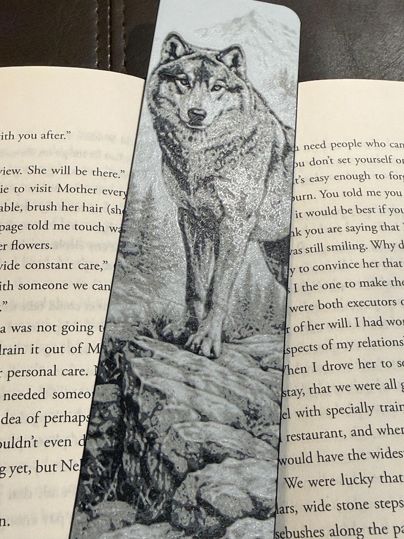 Puede incluir: Un marcap&aacute;ginas en blanco y negro con una ilustraci&oacute;n detallada de un lobo sobre una superficie rocosa, con una monta&ntilde;a de fondo. El marcap&aacute;ginas est&aacute; insertado en un libro, con texto visible en ambos lados.