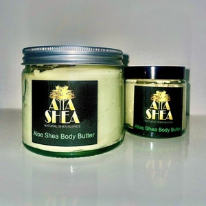 Pode incluir: Dois frascos de manteiga corporal de aloe e karité, um maior e outro menor. Ambos os frascos têm um rótulo verde com um logotipo de árvore dourado e o texto "AA SHEA NATURAL SHEA BLENDS Aloe Shea Body Butter".