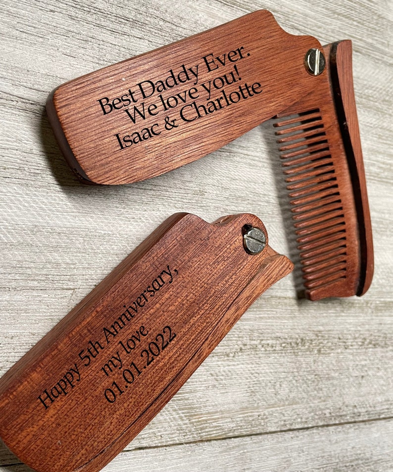 May include: A wooden folding comb with a personalized message: "Happy 5th Anniversary, my love 01.01.2022" on one side and "Best Daddy Ever. We love you! Isaac & Charlotte" on the other side.