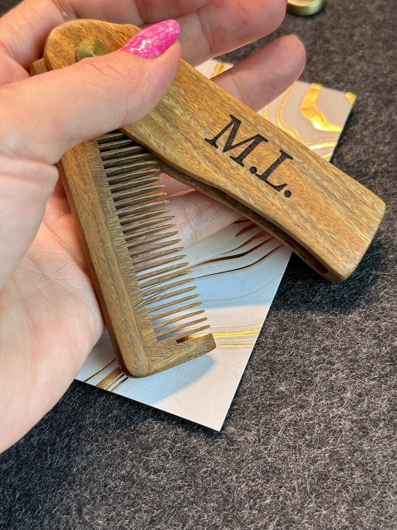May include: A wooden comb with a folding design. The comb has a brown wood finish and the words "M.L." are engraved on the handle.