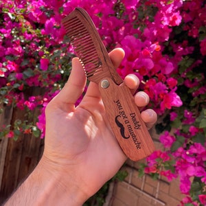 May include: A wooden comb with a mustache design and the text "Daddy you got a mustache".