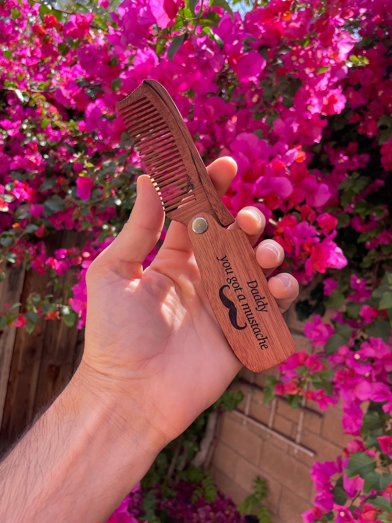May include: A wooden comb with a mustache design and the text "Daddy you got a mustache".