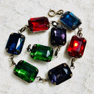 May include: A silver chain bracelet with eight faceted rectangular gemstones in red, green, and blue. The gemstones are set in silver.