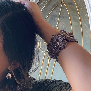 May include: A silver bracelet with intricate floral designs. The bracelet is made of filigree and has a delicate, feminine look.