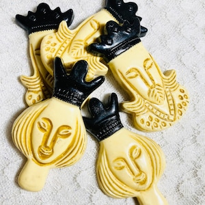 May include: Five vintage chess pieces made of ivory-colored plastic with black crowns. The pieces are a king, queen, and three pawns. The pieces are in good condition with some minor wear and tear.