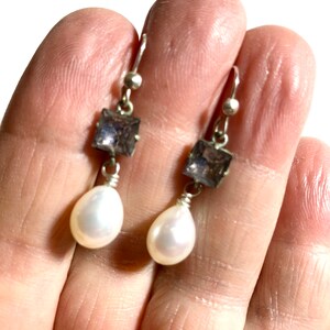 May include: Silver dangle earrings with a square shaped purple gemstone and a white pearl drop.