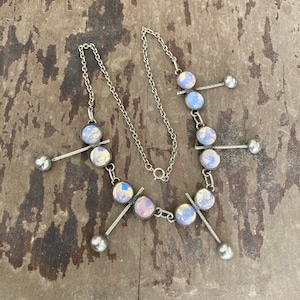 May include: A silver necklace with iridescent glass circles and silver balls hanging from the chain. The circles have a gold-toned design.