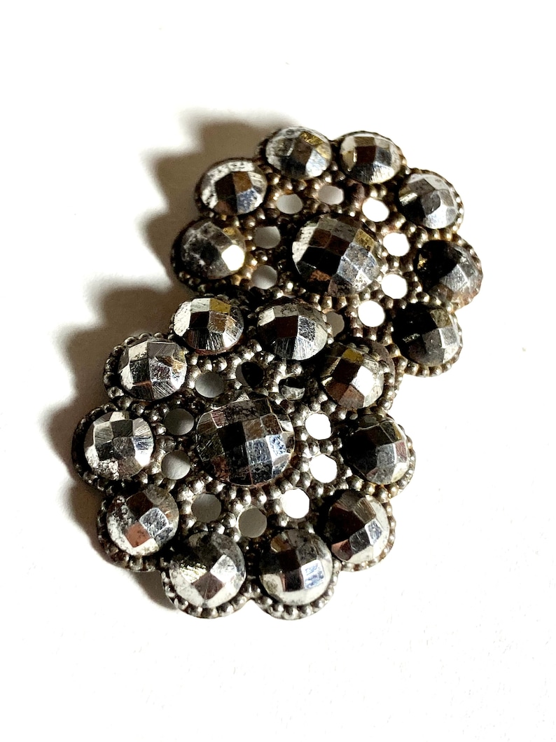 May include: Two silver-toned metal buttons with a decorative design of raised, faceted circles arranged in a circular pattern.