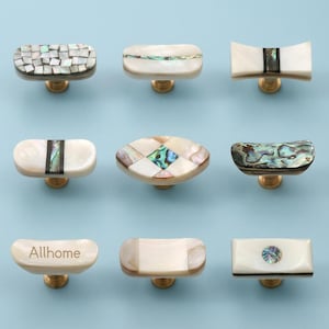 May include: Nine decorative cabinet knobs with brass bases. The knobs showcase diverse designs, such as mosaic, oval, and rectangular shapes, with iridescent abalone shell inlays. One knob has the word "Allhome" engraved.