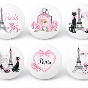 Peut inclure: Boutons décoratifs blancs avec des motifs parisiens. Chaque bouton présente une illustration différente, notamment la Tour Eiffel, un caniche, un flacon de parfum, un chat, des talons hauts et un vélo, le tout en rose et noir.