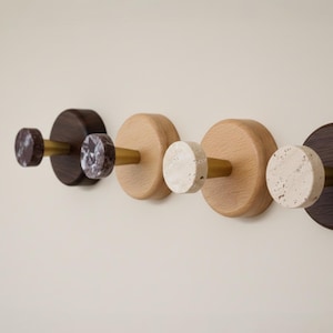 May include: Four wall hooks with a minimalist design. The hooks feature a combination of dark brown and light wood, with stone and brass accents. The hooks are mounted on a neutral-coloured wall.