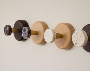 May include: Four wall hooks with a minimalist design. The hooks feature a combination of dark brown and light wood, with stone and brass accents. The hooks are mounted on a neutral-colored wall.
