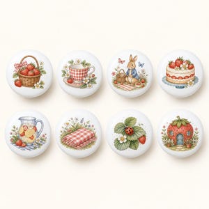 Peut inclure: Un ensemble de huit boutons de placard ronds en céramique blanche, chacun présentant une illustration colorée distincte incluant un panier de fraises, une tasse à carreaux, un lapin, un gâteau aux fraises, une carafe, une couverture, une coccinelle et une maison fraise.