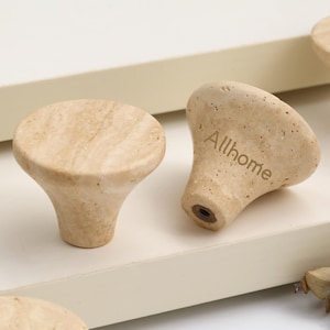 May include: Close-up of several light-colored, mushroom-shaped cabinet knobs. One knob is angled, revealing the word "Allhome" etched into the side. The knobs have a natural, textured appearance, suggesting a wood or stone material.