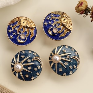 May include: Four celestial-themed decorative cabinet knobs. Two knobs feature a sun and moon design with a blue background, while the other two have a sunburst design with a pearl center and a dark teal background. Gold-tone metal accents.