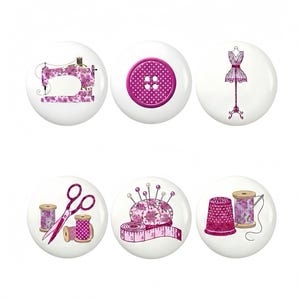 May include: Six white round buttons featuring sewing-related illustrations. The designs include a sewing machine, a button, a dress form, scissors, a pincushion with measuring tape, and a thimble with thread spools. The designs are in pink and purple.