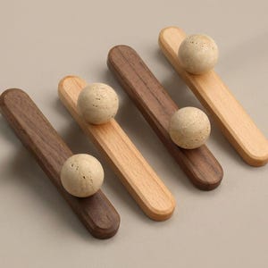 May include: Four wooden cabinet pulls with a ball-shaped handle. Two pulls are dark brown, and two are light brown. The handles are a light beige color. The pulls are arranged diagonally on a neutral background.
