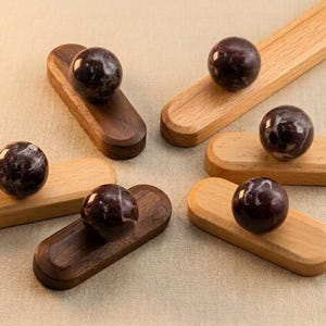 May include: Six decorative wooden coasters with a dark, marbled sphere on each. Three coasters are a light wood color, and three are a dark brown. The coasters are arranged on a neutral-toned surface.