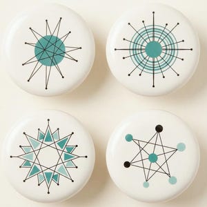 Puede incluir: Cuatro pomos de armario de cerámica blanca con diseños modernos de mediados de siglo. Cada pomo presenta un patrón geométrico diferente en color turquesa y negro, incluyendo diseños de estrella y radiales. Ideales para dar un toque retro a los muebles.