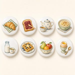 Pu&ograve; includere: Un set di otto bottoni rotondi in ceramica con illustrazioni di articoli per la colazione, tra cui un cornetto, pane tostato con marmellata, una teiera con tazza, avena con banane, latte e caff&egrave;, un waffle con mirtilli, frutta in una ciotola e un uovo.