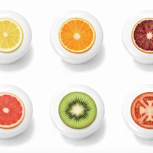 May include: Six white cabinet knobs with fruit slice designs. The knobs feature a lemon, orange, blood orange, grapefruit, kiwi, and tomato. Each knob has a circular fruit design on a white background.