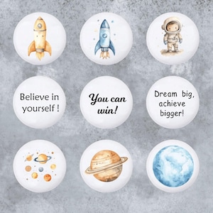 May include: Nine white round stickers with different space-themed illustrations and inspirational quotes. The stickers feature a blue and white rocket, a yellow and orange rocket, an astronaut, a solar system, a planet with rings, a blue planet, and three inspirational quotes: "Believe in yourself!" "You can win!" and "Dream big, achieve bigger!"
